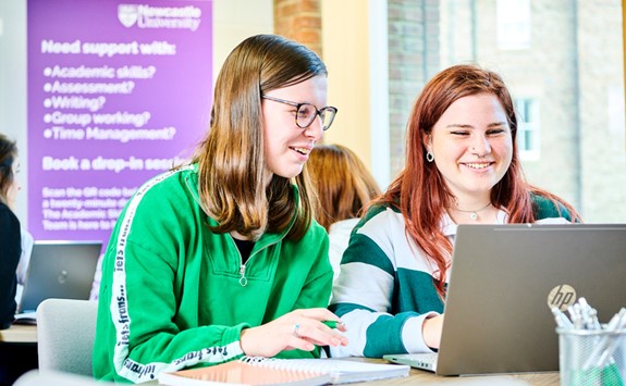 Two students sitting together sharing a laptop with banner promoting academic skills behind them